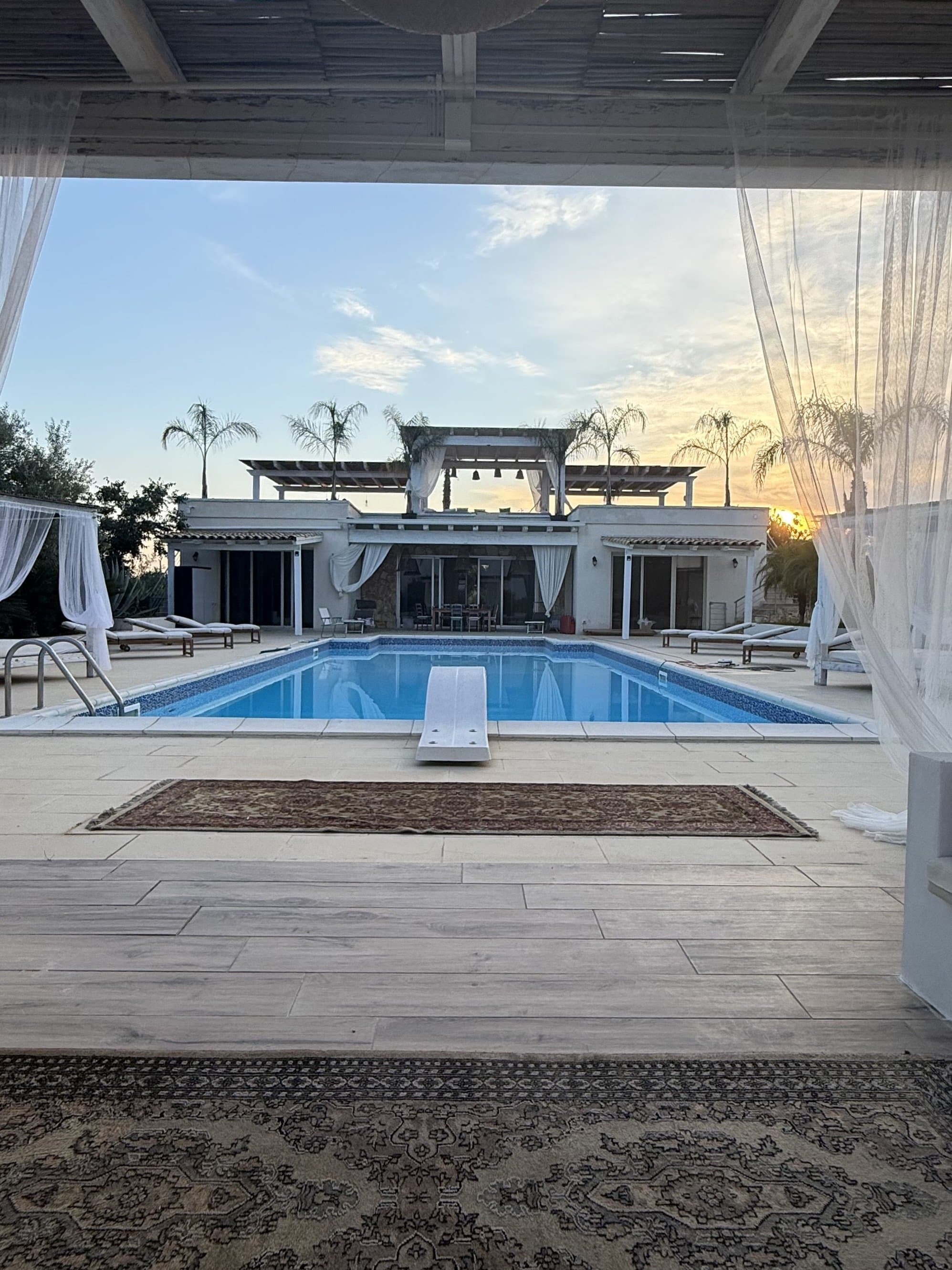 Vue depuis le salon extérieur sur la piscine et la villa au coucher du soleil